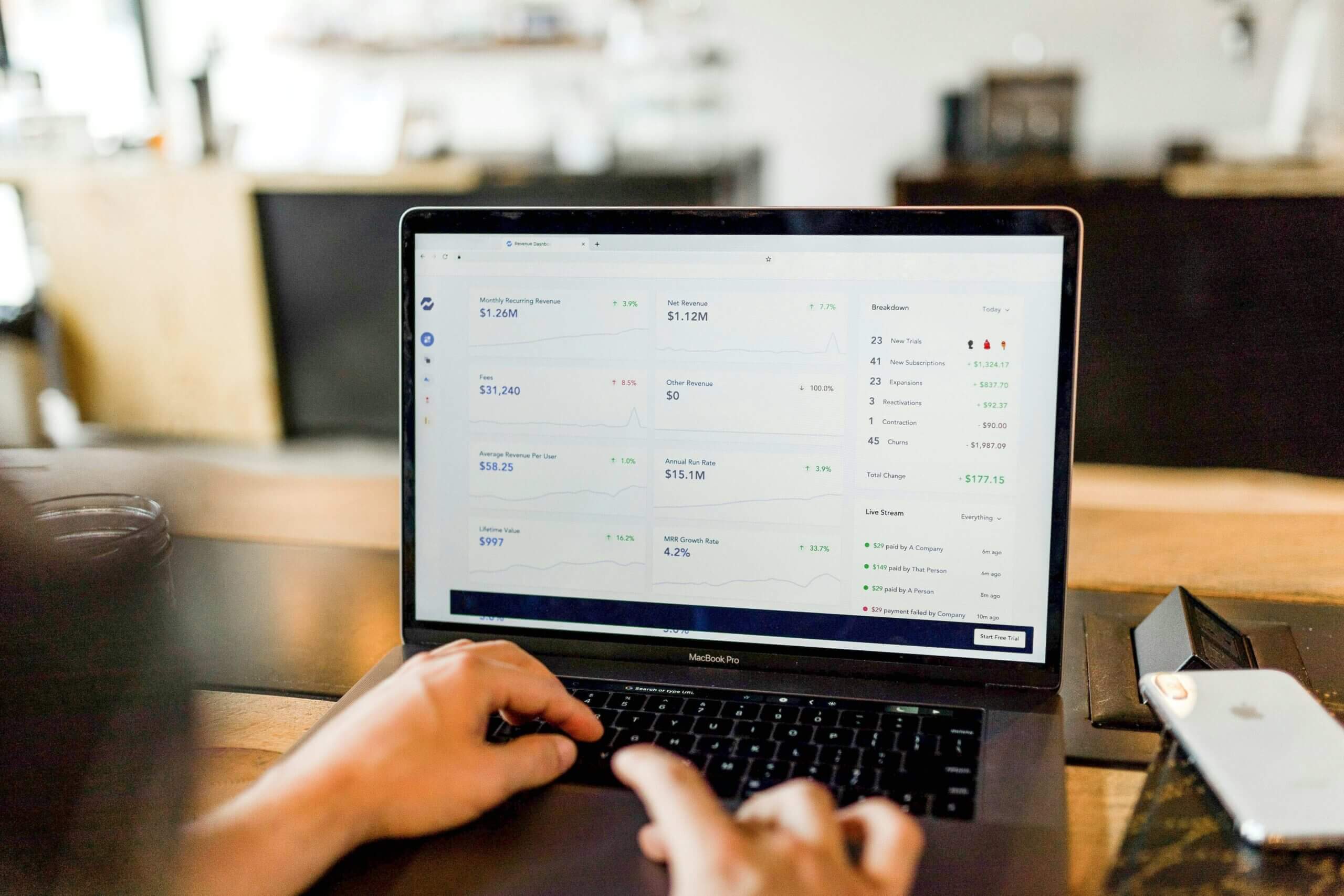 Laptop on wooden table displaying a management dashboard, with user engaged in typing.