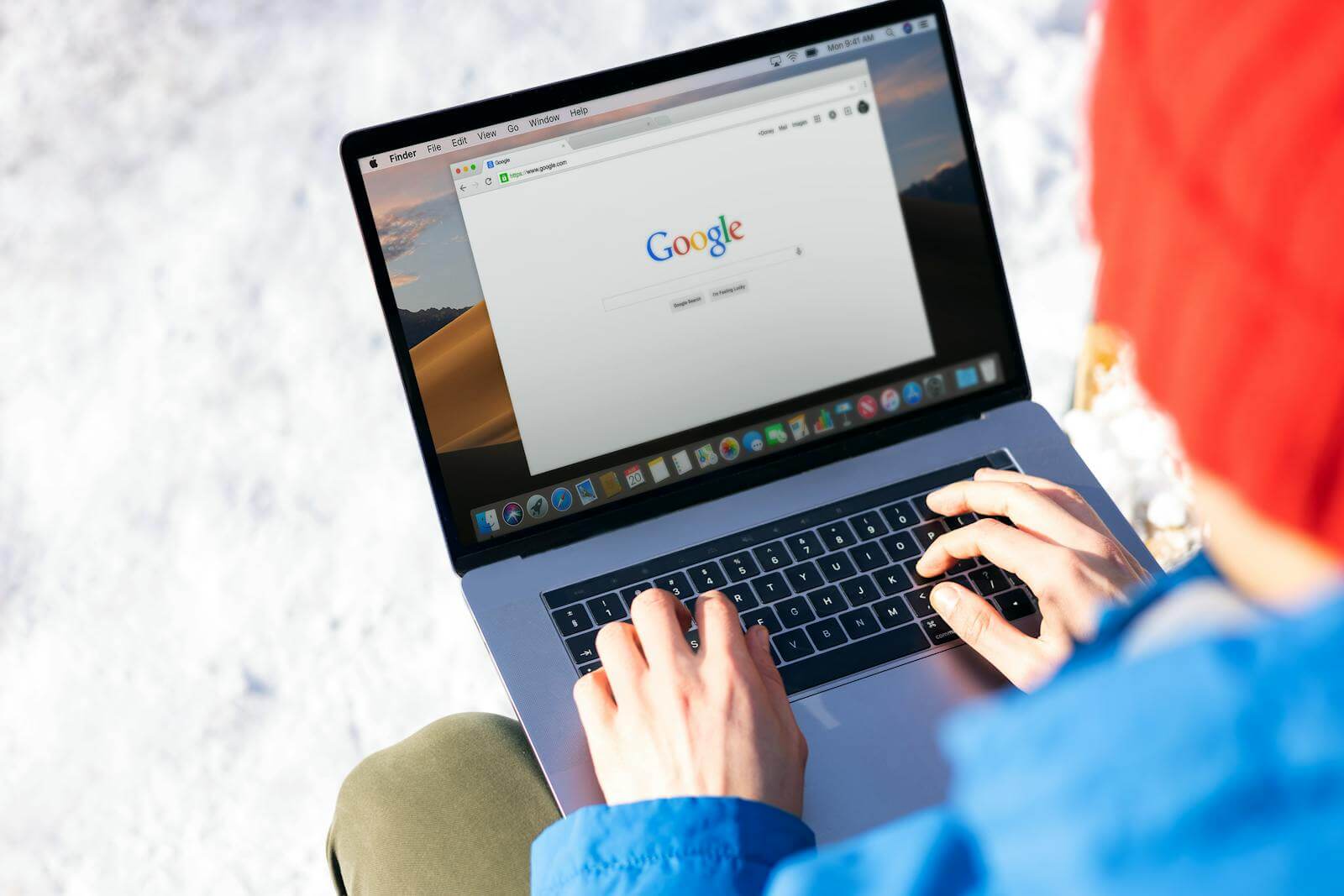 Person typing on laptop in snow, blending technology with a peaceful winter landscape.