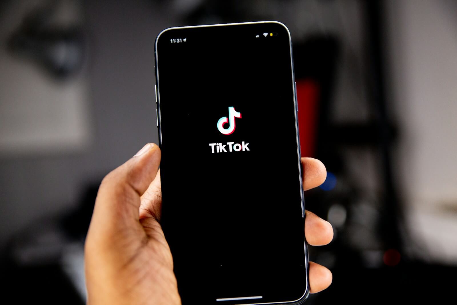 Close-up of hand holding a smartphone displaying the TikTok app logo.